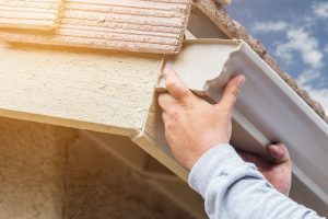 Worker Attaching Aluminum Rain Gutter to Fascia of House.